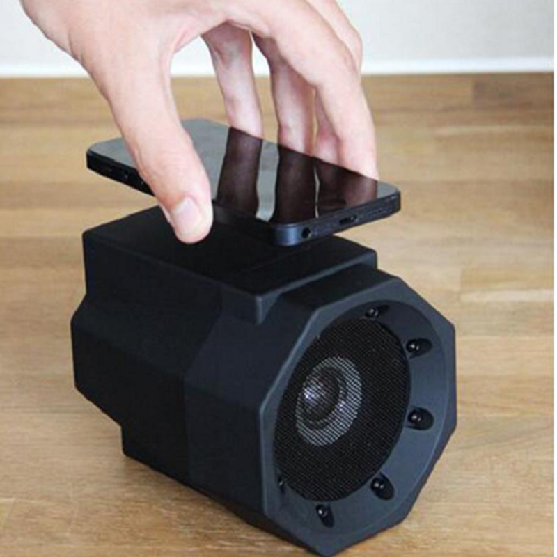 Black portable speaker with a hand placing a smartphone on top, on a wooden surface.