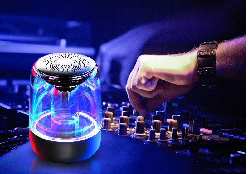 Colorful LED light show on a small cylindrical device with a person operating DJ equipment in the background.